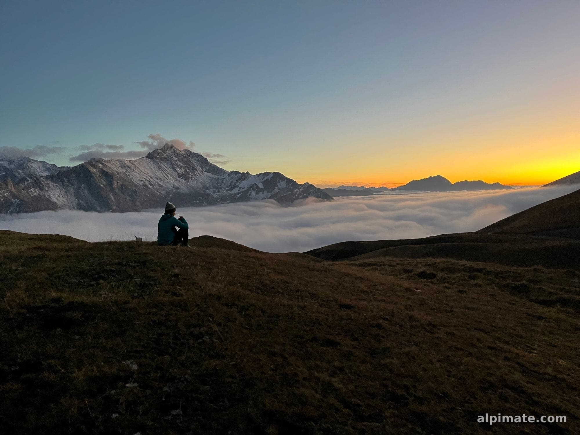 Chloé, cofondatrice d'Alpimate, assise face à une mer de nuages et des sommets enneigés à la lumière dorée